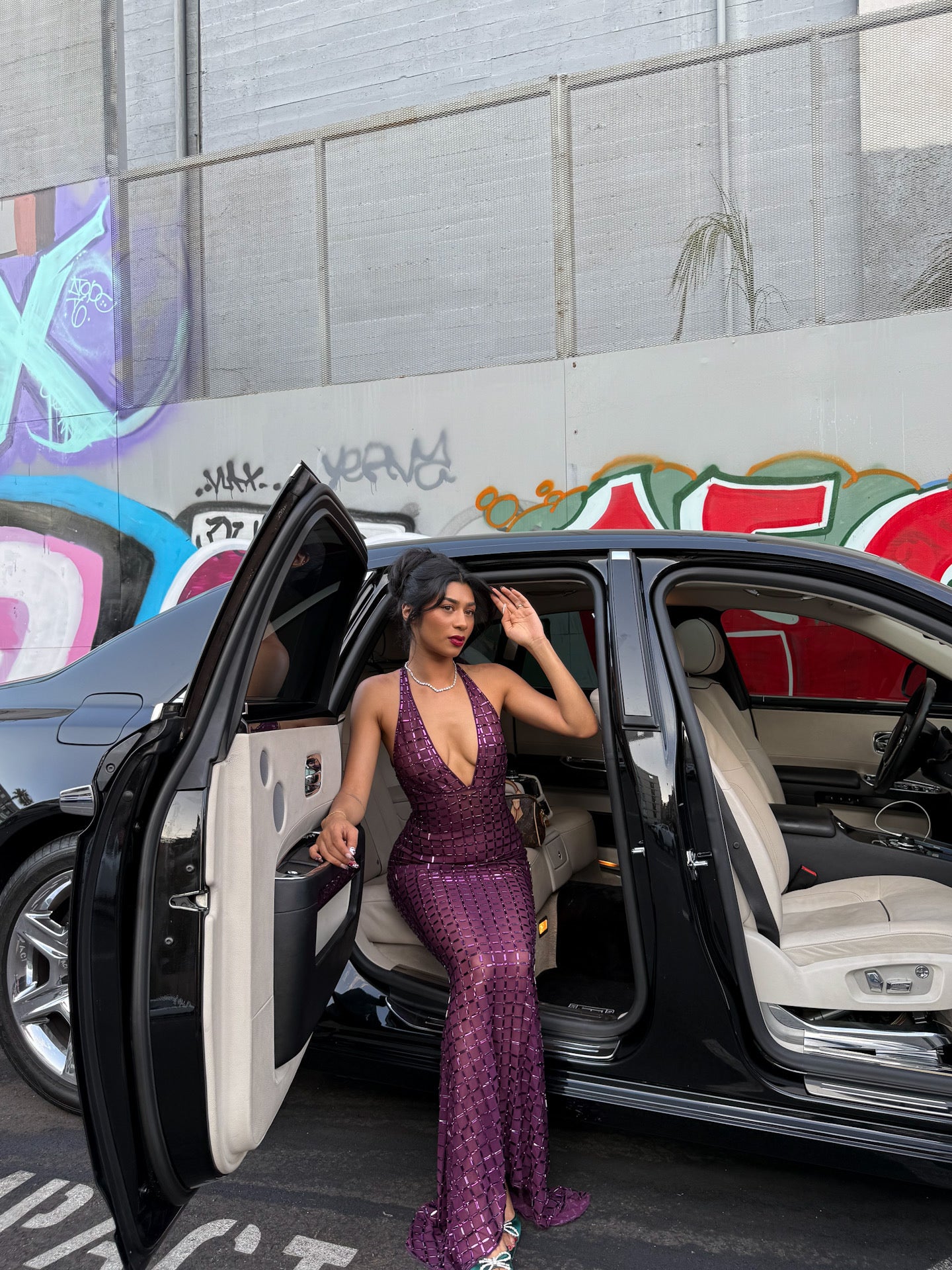 Woman in a purple dress getting out of a car with graffiti in the background