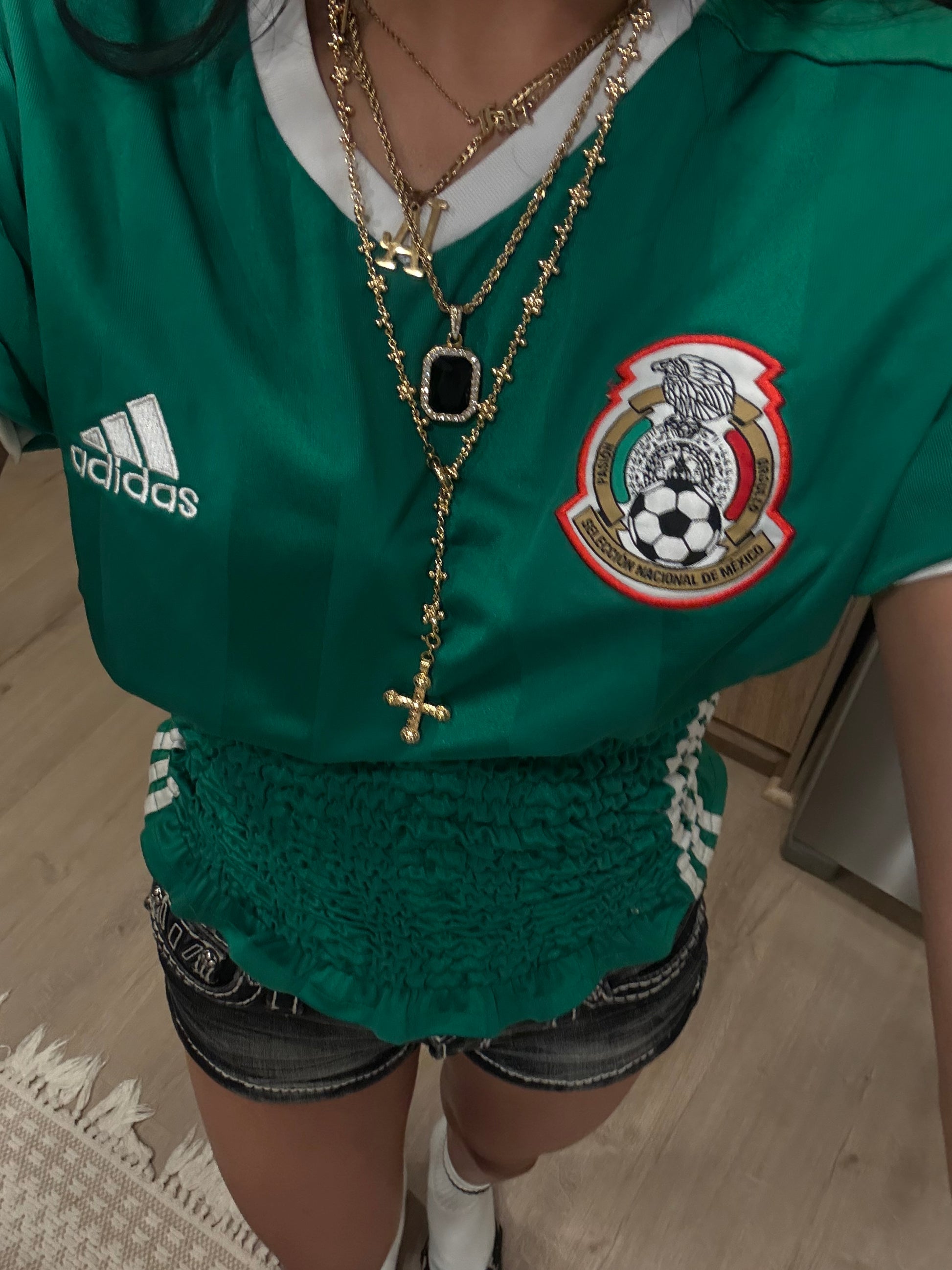 Person wearing a green Adidas sports jersey with a logo, sitting on a chair.