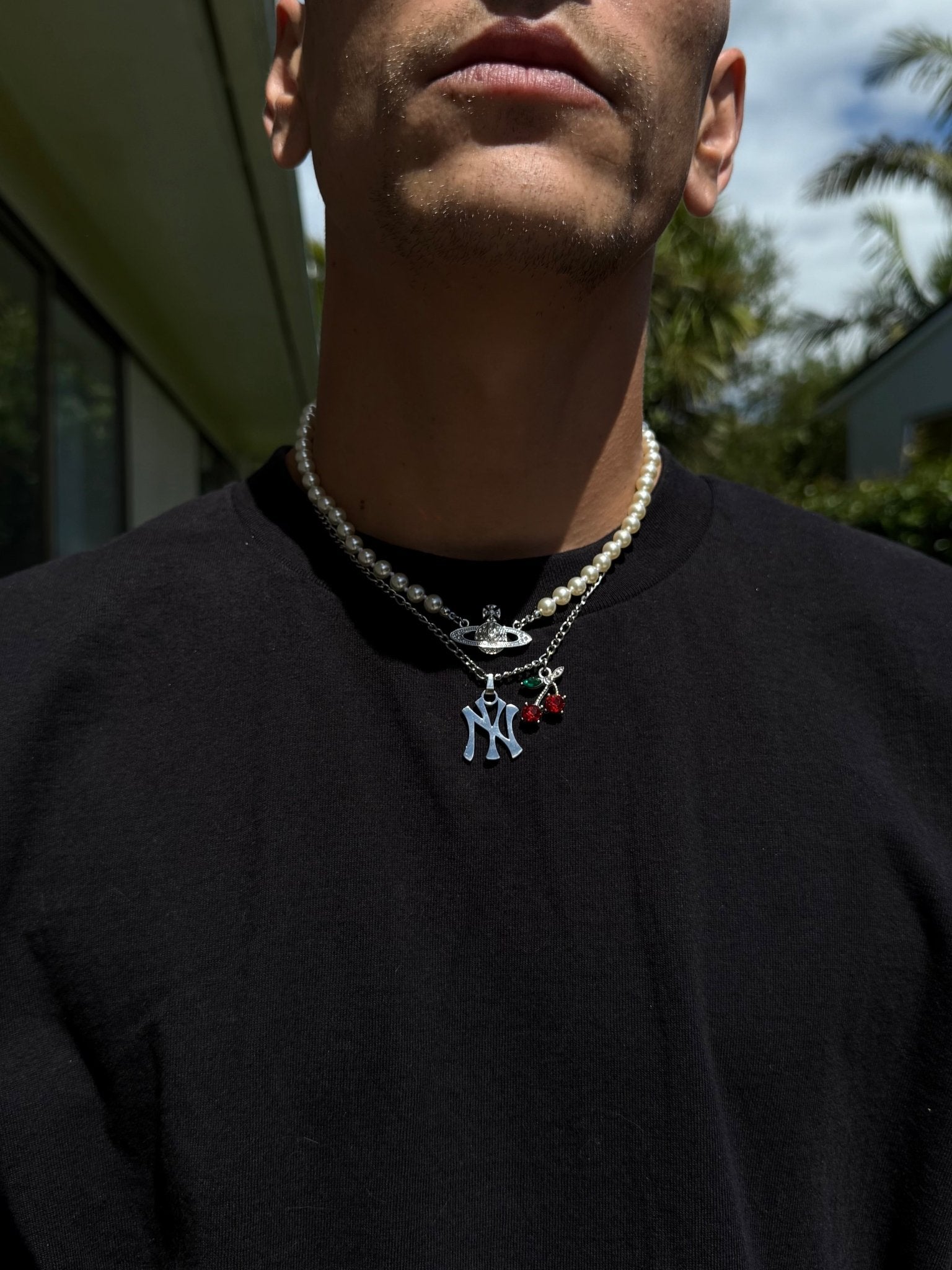 Person wearing a black shirt with a necklace featuring multiple pendants outdoors.