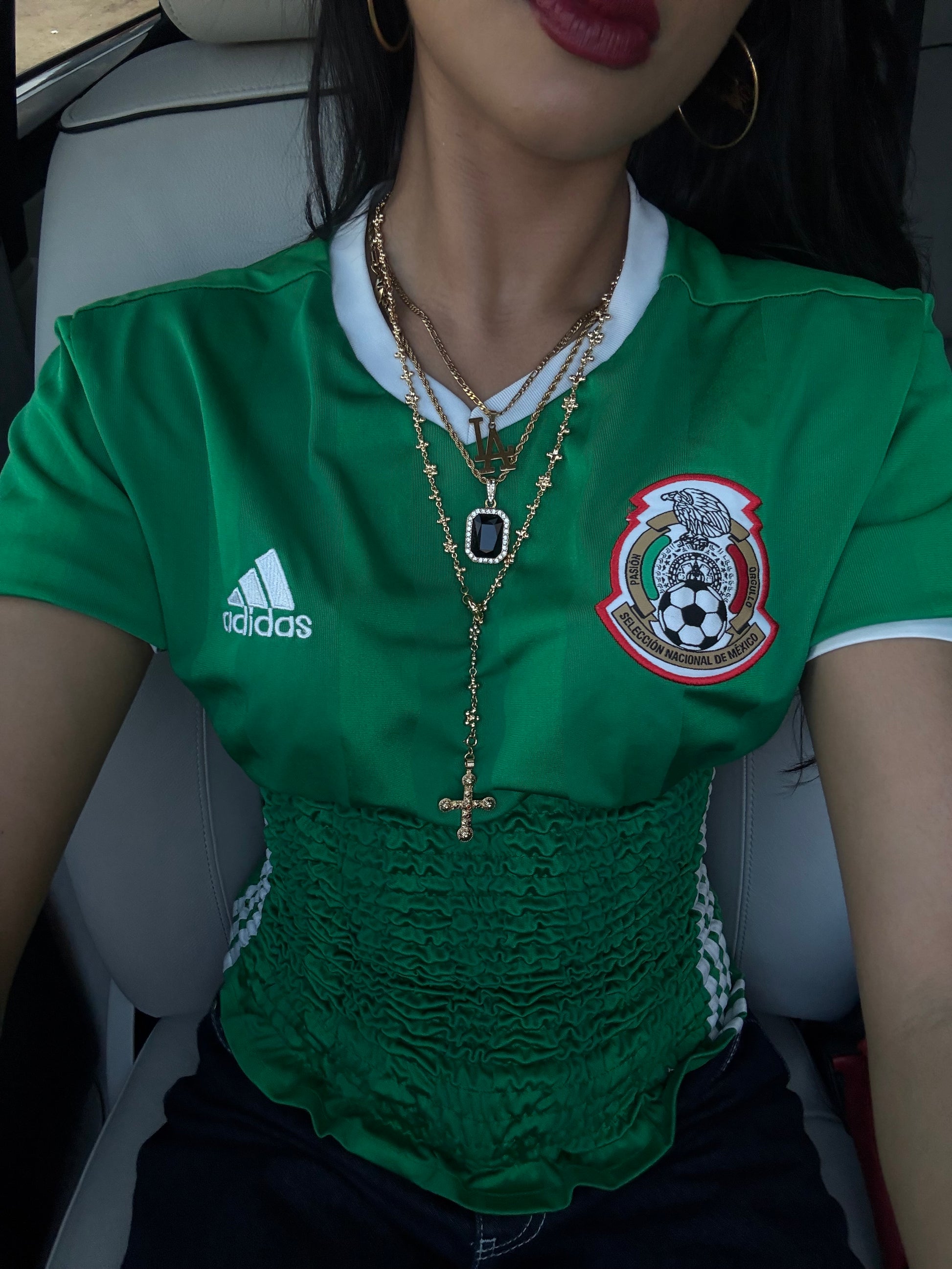Person wearing a green Adidas jersey with a logo, sitting in a vehicle.