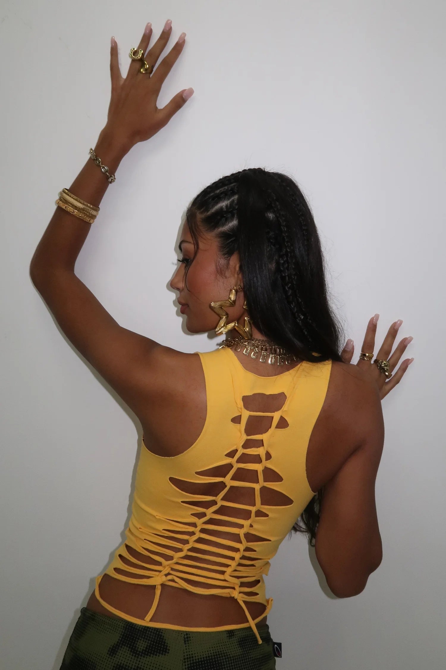 Woman wearing a yellow sleeveless top with a unique design, posing against a plain background.
