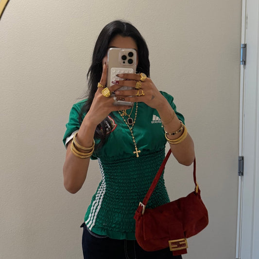 Person wearing a green Adidas top with gold jewelry and a red bag, taking a mirror selfie.
