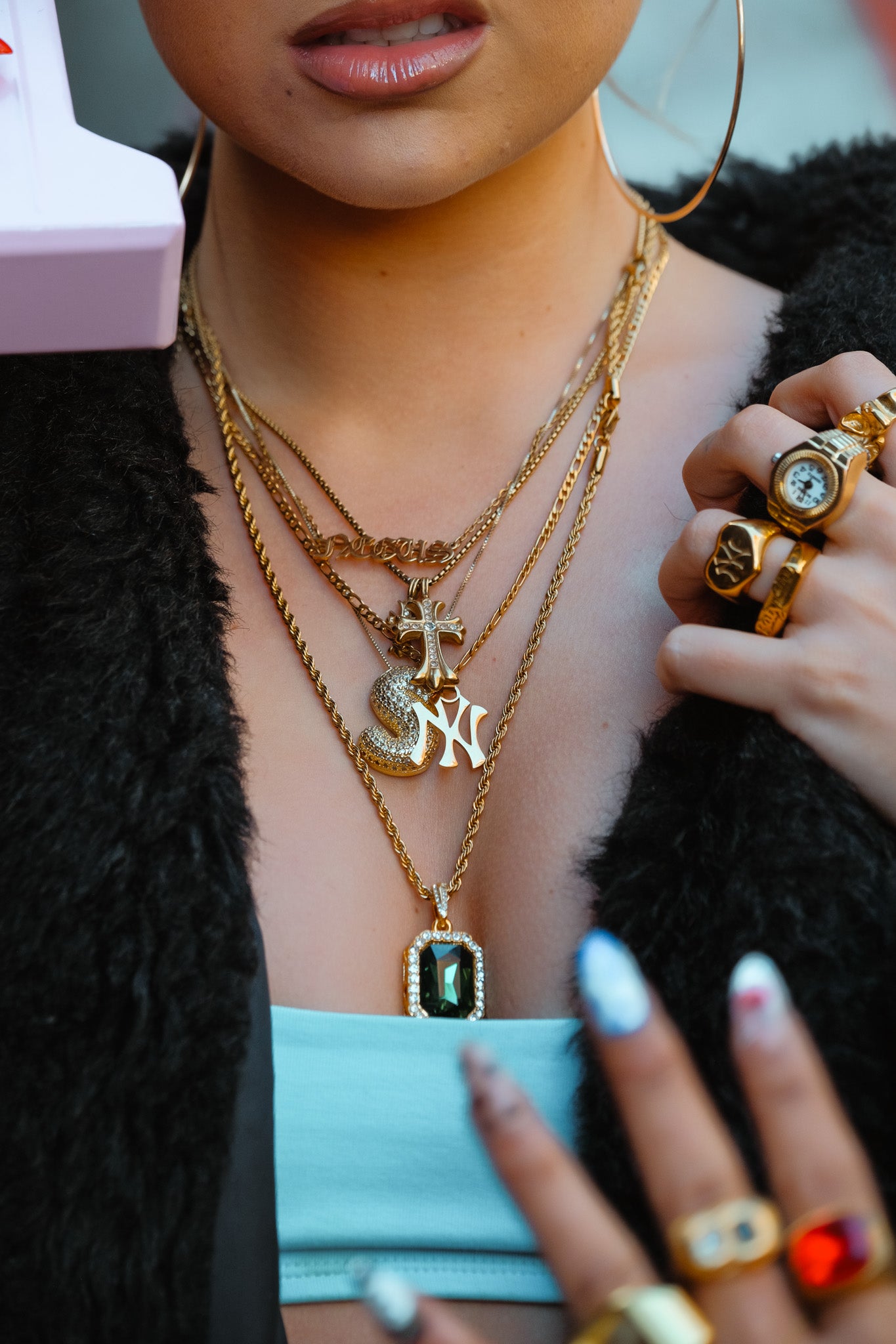 Close-up of a person wearing multiple gold necklaces and rings with colorful gemstones.