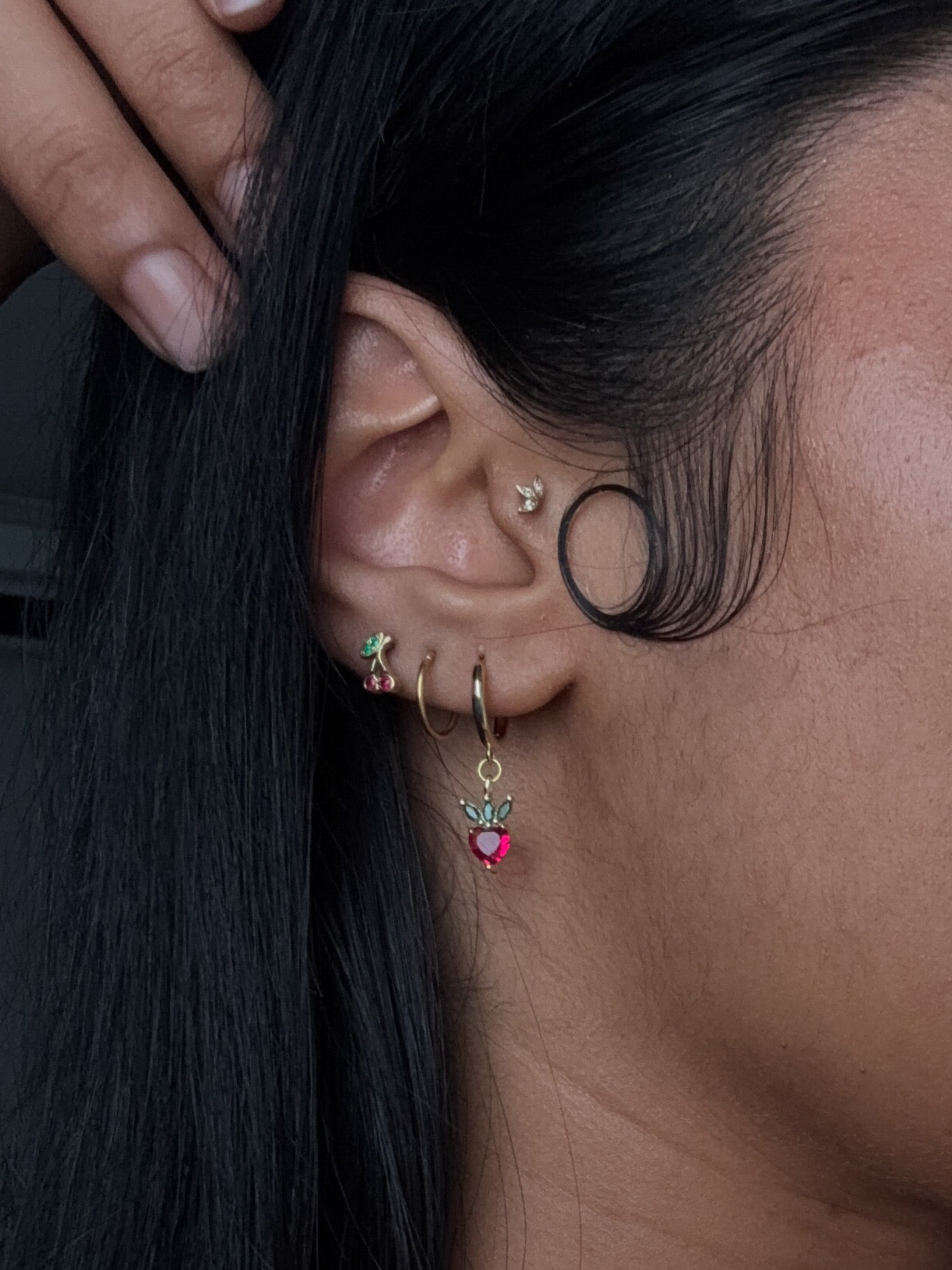 A collection of gold-colored mini hoop earrings with various colorful fruity loop dangle charms attached to each.